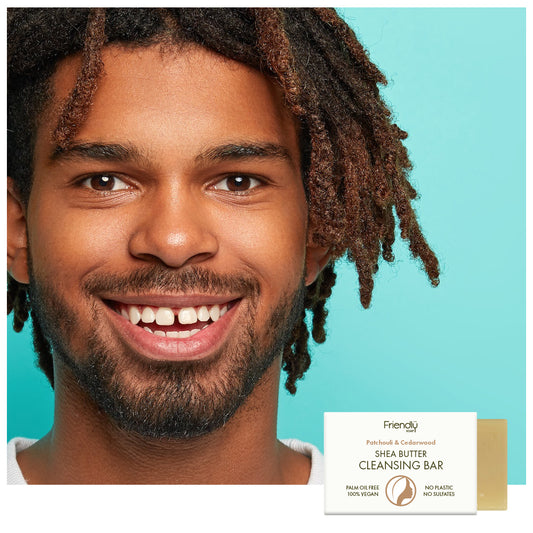 A smiling man with dark dreadlocks is shown against a bright turquoise background, with a small product box labeled Friendly Shea Butter Cleansing Bar in the lower right corner.