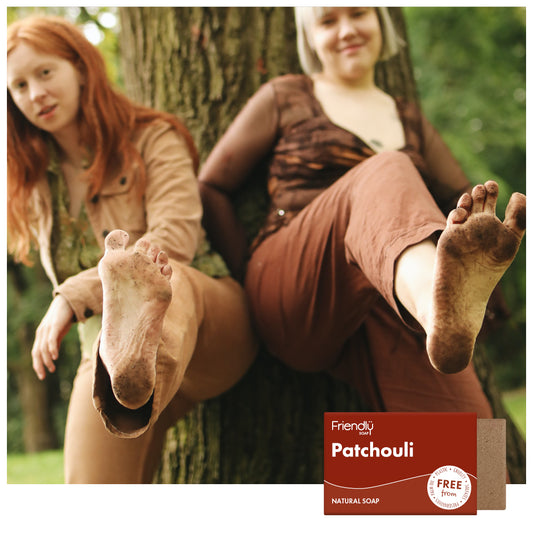 Two hippy women outdoors showing bare dirty feet with a 'Friendly Soap' patchouli and sandalwood bar soap in the foreground.