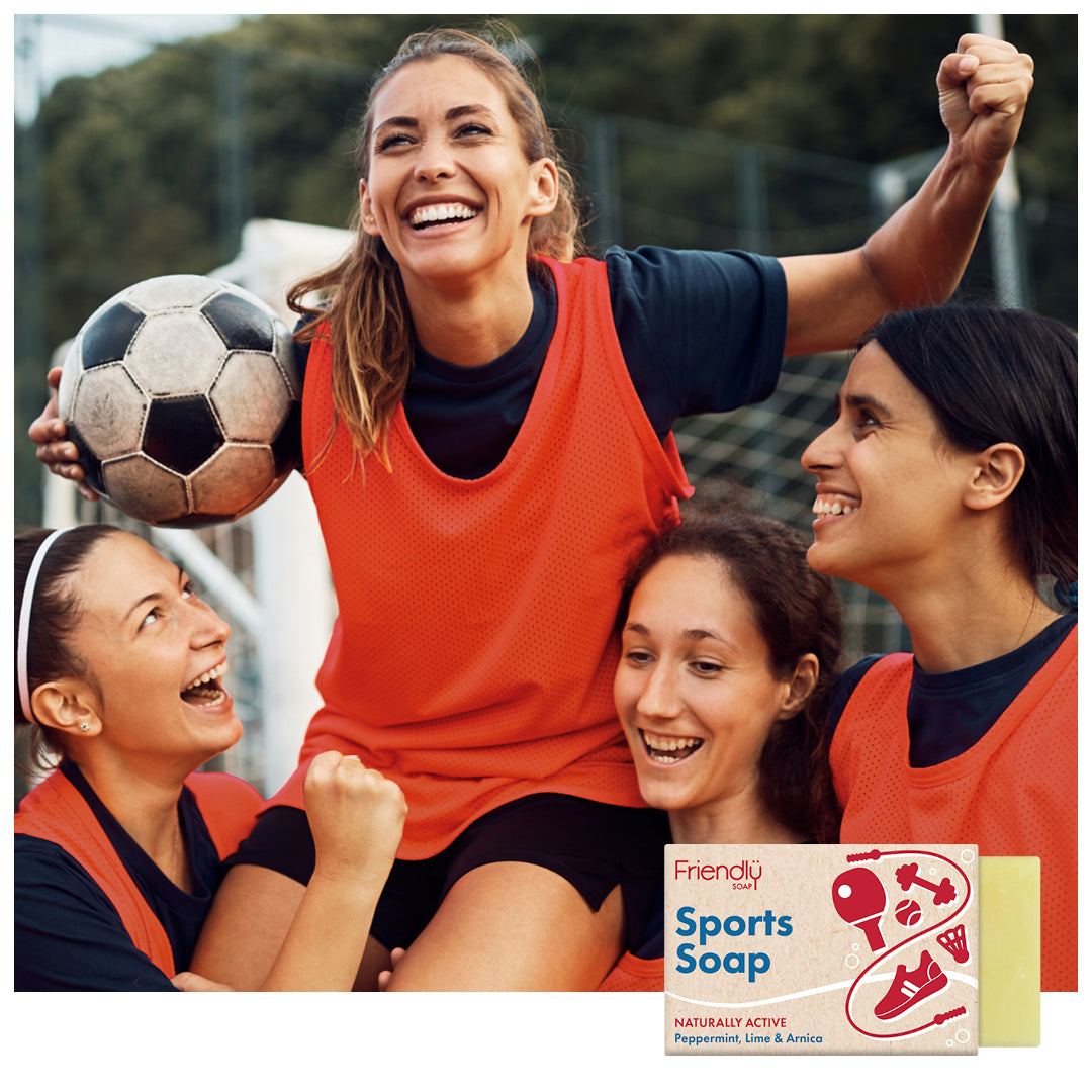 Group of female football players celebrating with a ball, featuring Friendly Soap sports soap packaging.