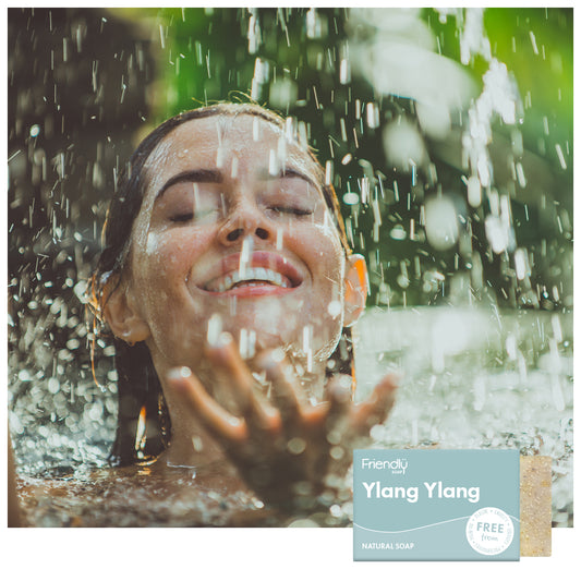 Woman under a waterfall with a 'Friendly Soap Ylang Ylang' bar displayed.