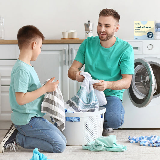 Man and boy sorting laundry in a kitchen with a box of laundry powder in the background.