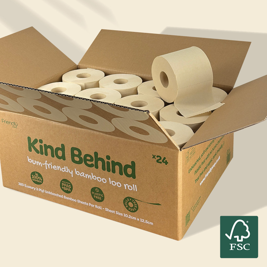 An open brown cardboard box filled with bamboo toilet paper rolls, with the front label reading 'Kind Behind' and a green FSC logo in the lower right corner.