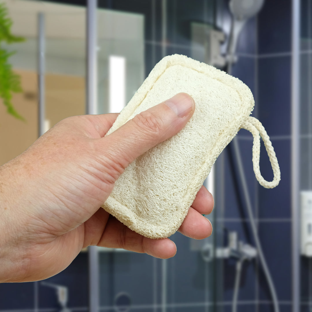 hand holding small, wet loofah outside of a blue shower unit