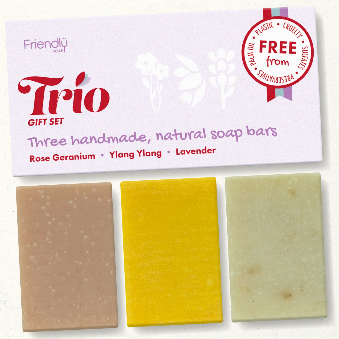 A gift set of three handmade natural soap bars from Friendly Soap, labeled Trio, featuring rose geranium, ylang ylang, and lavender scents. The soaps are displayed below their white packaging card, which includes a 'Free from' cruelty and plastic seal.