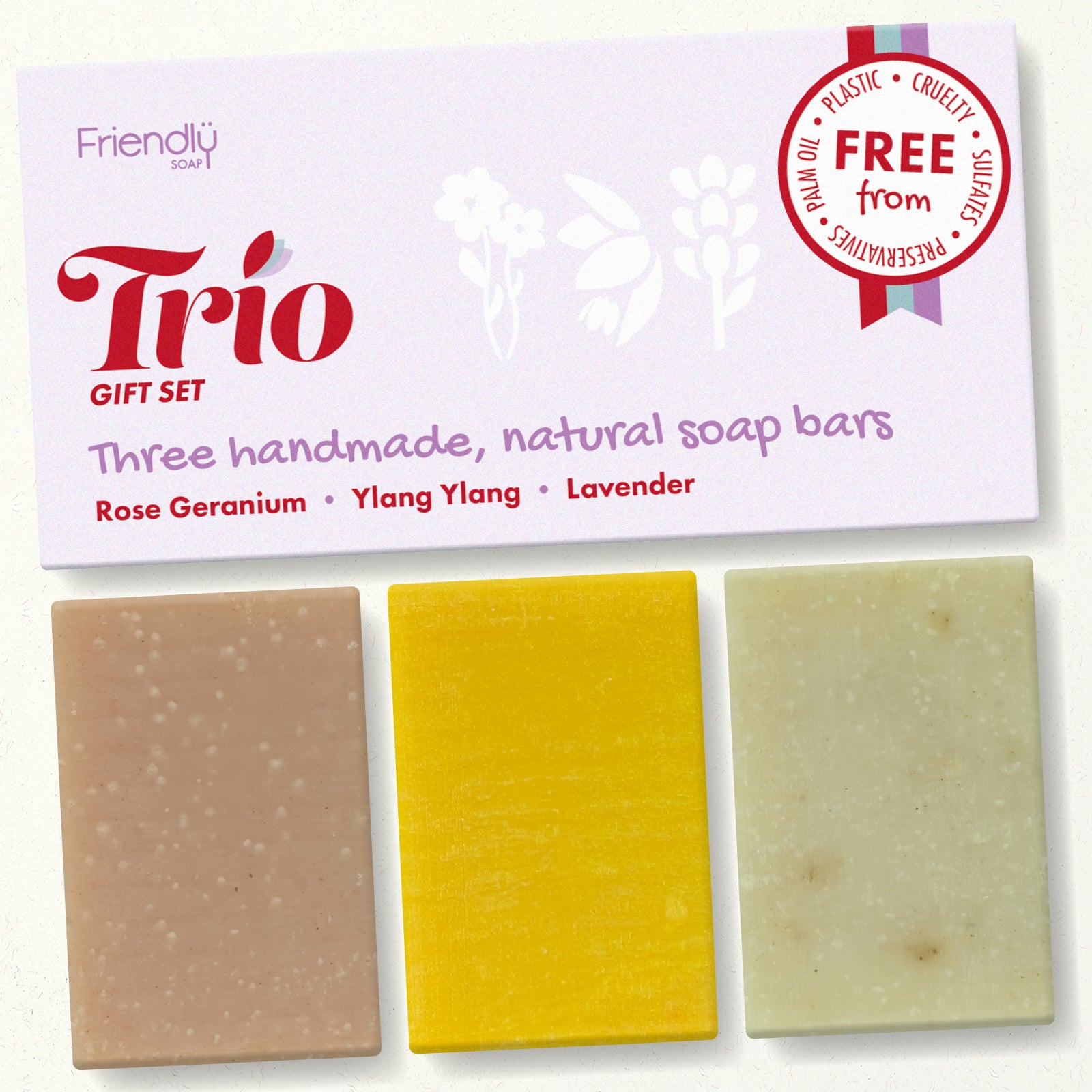 A gift set of three handmade natural soap bars from Friendly Soap, labeled Trio, featuring rose geranium, ylang ylang, and lavender scents. The soaps are displayed below their white packaging card, which includes a 'Free from' cruelty and plastic seal.
